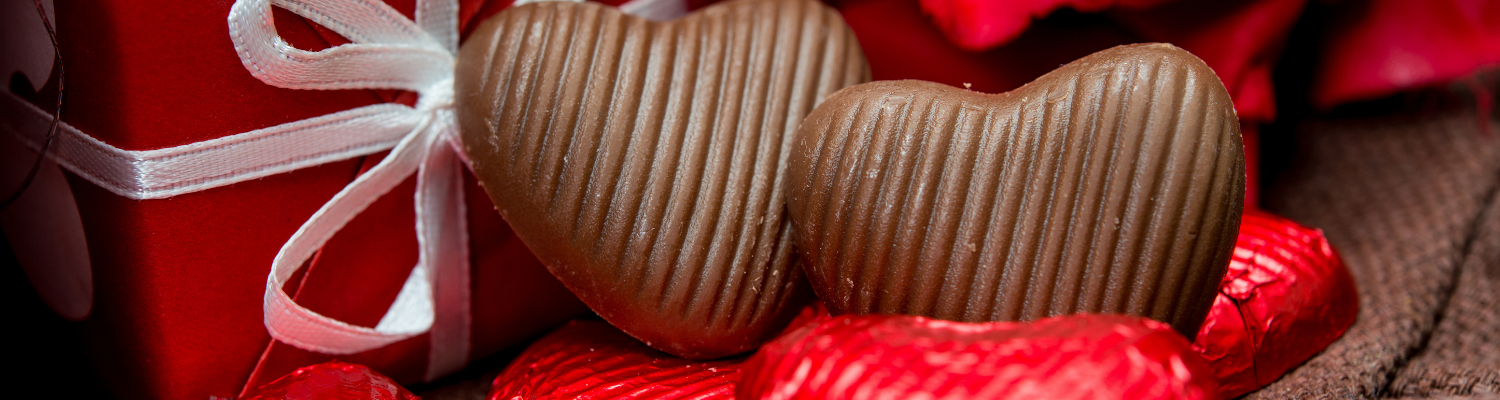 Schokoherzen und rote Geschenkverpackung – charmantes Bild für klassische, süße Aufmerksamkeiten wie Schokolade und Leckerli als Weihnachtsgeschenke für Hund und Halter.