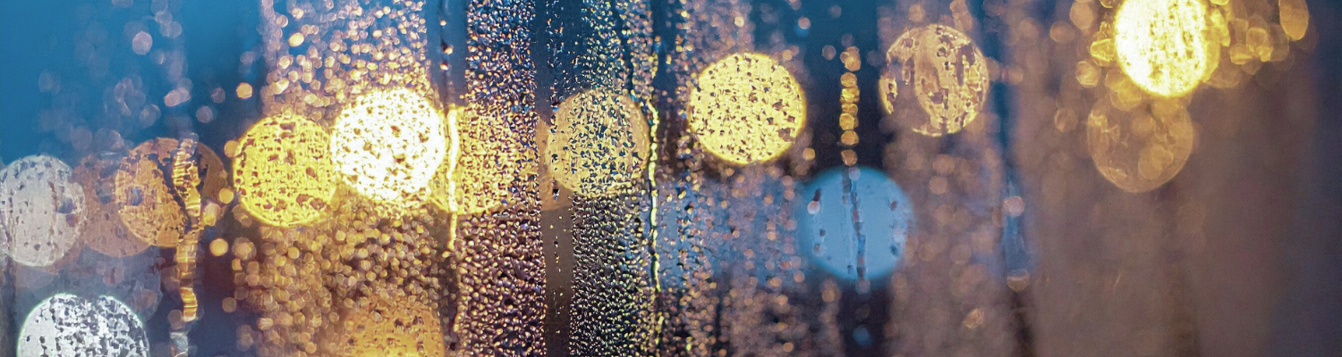 Unscharfe Lichtpunkte hinter einer Glasscheibe mit Wassertropfen