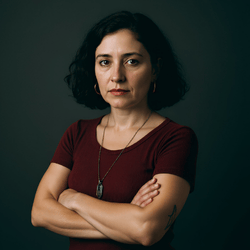 Venus (2021). Eine Frau Mitte 40 mit mittellangem dunklen Haar, in einem weinroten T-Shirt vor dunklem Hintergrund. Ihr Blick ist ruhig, ernst und voller spiritueller Tiefe.