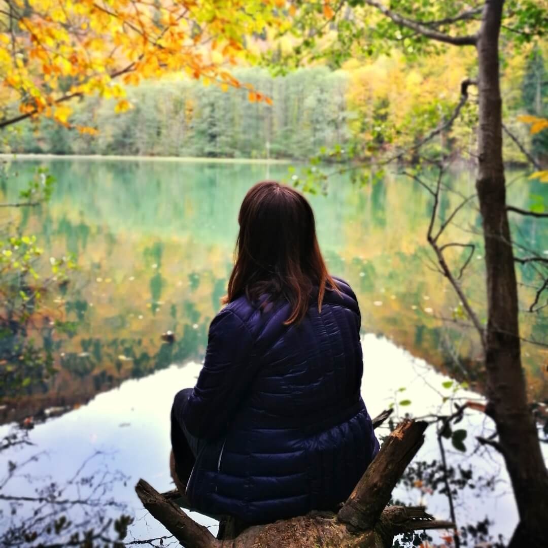 Frau sitzt am Wasser auf dem Baumstamm